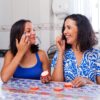 mãe e filha aplicando Pomada Minancora no rosto e sorrindo na cozinha.