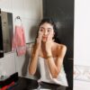 Menina jovem aplicando produtos Minancora na face em um banheiro