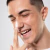homem sorridente aplicando creme branco no nariz como parte de uma rotina de skincare minimalista