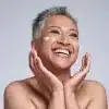 Pessoa madura sorridente com creme facial nas bochechas, representando cuidados com a pele e autoestima no skincare 50 anos.