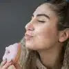 Pessoa com expressão de desejo segurando um donut rosa com confeitos brancos próximo ao rosto, ilustrando o impacto do açúcar na pele e os efeitos do consumo excessivo de doces na saúde facial.