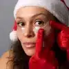 Pessoa com chapéu de Natal e luvas vermelhas aplica patches de glitter sob os olhos como parte da rotina de cuidados com a pele para festas de fim de ano.