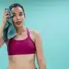 Mulher usando top esportivo magenta segura toalha teal no rosto após treino, representando cuidados com a pele oleosa depois de treinar.
